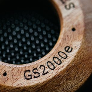 Åben hi-fi hovedtelefon Grado GS2000e i lyst træ med perforerede sorte ørepuder, tæt på billede af den graverede logokappe
