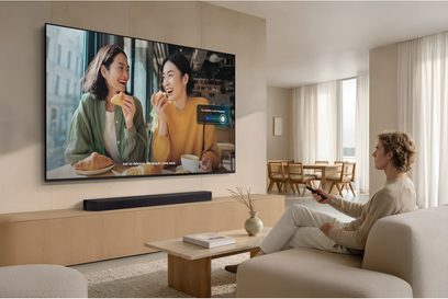 Samsung TMR85R85H fladskærms-tv monteret på væggen i en moderne stue, set forfra med fjernbetjening