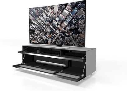 Sort TV-møbel med 2 skuffer, 2 nicher, i glas og metal, under en stor fladskærm der viser et tætpakket luftfoto af skyskrabere