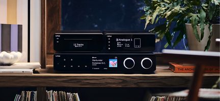 Černý hi-fi systém Cyrus se síťovým přehrávačem a stereo zesilovačem, dvojité podsvícené ovladače na dřevěném stolku