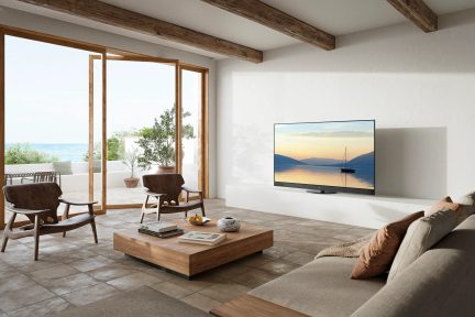 Salón moderno con vista al mar, sofá beige, mesa de centro de madera, 2 sillones, televisión, ventanales, plantas