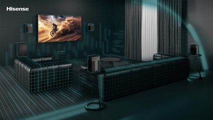 Perspektivisk visning af en virtuel stue med mørkegrønt ternet gulv, sort læderhjørnesofa, vægmonteret tv med motocross-scene, surroundhøjttalere og sofabord
