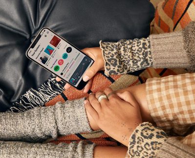 Smartfón s aplikáciou Spotify, ruky v leopardom pulóvri a sivom svetri na oranžovej vzorovanej deke