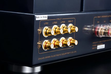 Nærbillede i trekvart vinkel af bagsiden på et sort metal audio-kabinet, udstyret med otte guldbelagte RCA-stik med hvid isolering, arrangeret i to rækker og omgivet af serigraferede mærkater