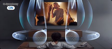 Großer schwarzer Wandfernseher mit schmalem, dunklem Metallrahmen, Flachbildschirm zeigt einen Sänger, Rückansicht leicht von oben auf einen sitzenden Zuschauer, bläuliche Spiral-Animationen deuten die Schallausbreitung im Wohnzimmer an