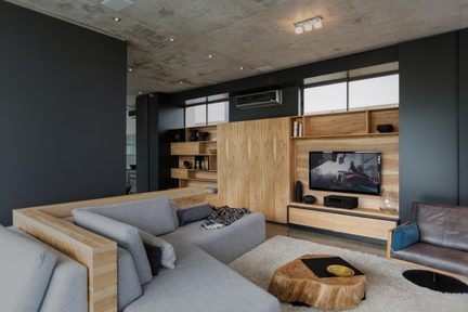 Modern vardagsrum med grå hörnsoffa, TV‑vägg i ljus trä och soffbord av naturlig trädstam på beige matta
