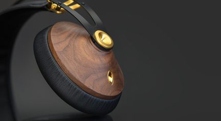 Nærbillede i trekvart vinkel af ørekoppen på et headset, rund skal i poleret, åretegnet brunt træ, tyk pude i sort kunstlæder, slankt bøjle i mat sort metal og gyldne detaljer