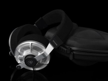 Black and silver headphones in metal and foam, open-back ear cups, padded headband, three-quarter view, next to a zippered case