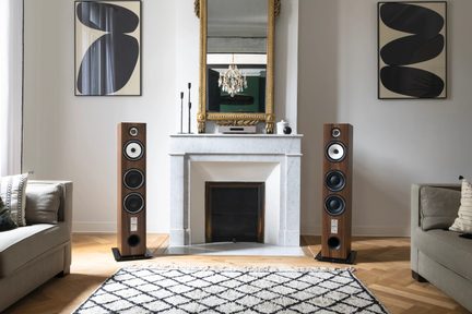 Par de altavoces de columna con acabado en madera marrón, tweeter dorado, altavoz de medios blanco, dos woofers negros y puerto bass réflex circular en la parte inferior, colocados sobre bases negras, vista frontal