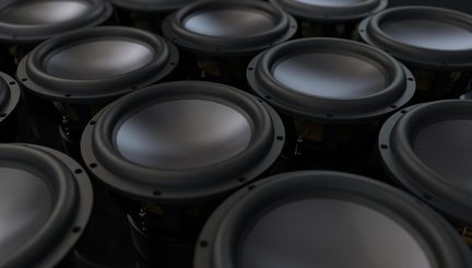 Gros plan en perspective sur plusieurs haut-parleurs ronds noirs, cônes gris texturés en métal et suspensions en caoutchouc