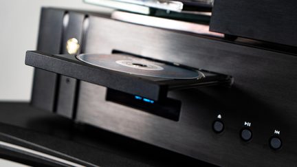 Must metallist musta harjatud viimistlusega CD-mängija, avatud sahtel plaadiga, ümmargused nupud ja sinine ekraan, vaade kolmest veerandist