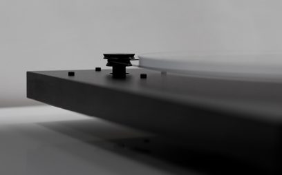 Rektangulær sort pladespiller med tonarm, set fra en skrå vinkel forfra på en ensfarvet grå baggrund
