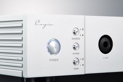 Vista ravvicinata del pannello frontale in alluminio argento del preamplificatore per cuffie Cayin IHA-8, con alette di ventilazione laterali, pulsante circolare di accensione con alone blu, tre mini-selettori metallici Source, Hyper e Gain e presa jack 6,3 mm 6.3SE