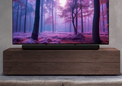 Sony Bravia Theatre Bar 8 juoda garso juosta po plokščiaekraniu televizoriumi, rodančiu violetinį mišką, tamsaus medžio baldai, pilka siena