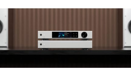 Hi-fi-set met twee elementen in mat wit aluminium, frontaal zicht, bovenste apparaat met centraal kleurenscherm, aan/uit-knop links en grote zwarte getextureerde draaiknop rechts, onderste apparaat minimalistisch met slechts één ronde knop links, units gescheiden door kleine metalen voetjes