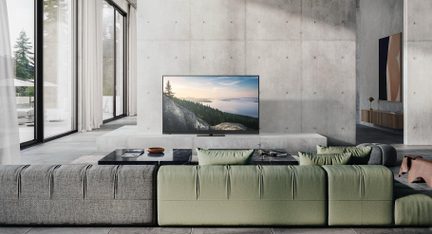 Bright contemporary living room, green and gray modular fabric sofa seen from the back, rectangular black stone coffee table, and flat-screen TV placed on a low concrete stand in front of a raw concrete wall