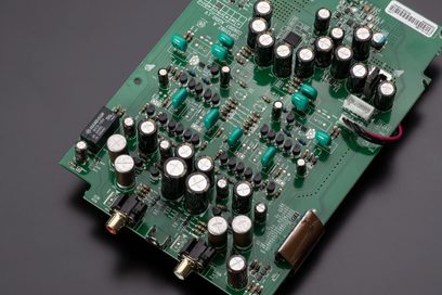 Placa de circuito impresso verde com componentes eletrônicos, capacitores cilíndricos prateados e pretos, close-up visto de cima
