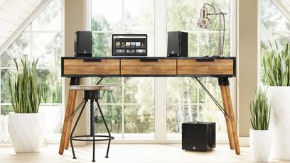 Subwoofer SVS 3000 Micro negru lucios pe un birou de lemn cu boxe, monitor, tastatură, mouse și plante verzi