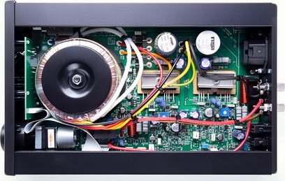 Sisäkuva avoimesta Rega io -stereovahvistimesta, jossa näkyy elektroniset komponentit vihreällä piirilevyllä