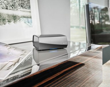 Denon HEOS Link HS2 sort netværksaudioafspiller, set forfra, placeret på et træbord foran et vindue