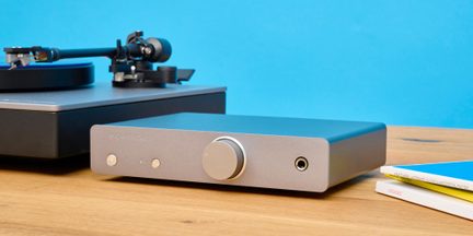 Hi-fi zesilovač Cambridge v hliníkově šedé barvě s velkým předním otočným ovladačem vedle gramofonu na dřevěném stole