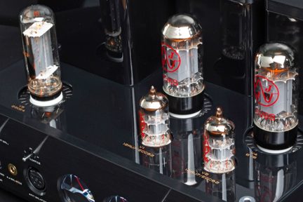 Vista dall’alto sul telaio metallico nero lucido di un amplificatore a valvole, primo piano che mostra diversi tubi di vetro con base nera e filamenti incandescenti arancioni