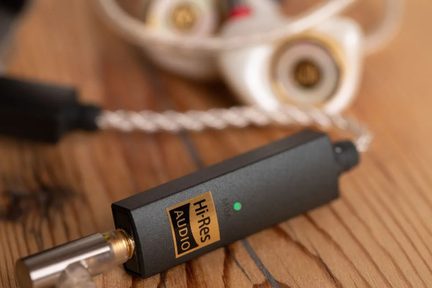Kompakt sort mat metal-lydadapter med gyldent "Hi-Res AUDIO"-mærkat, grøn LED-indikator og forgyldt jackstik, set tæt på i vinkel på en træoverflade