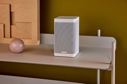 Compacte witte connected speaker op beige plank, olijfgroene muur, eigentijdse minimalistische decoratie