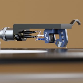 Un braccio di giradischi con una testina blu recante l'iscrizione "ortofon", cavi visibili e uno sfondo beige uniforme