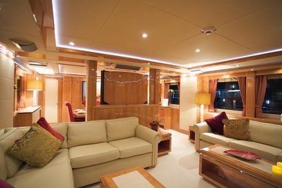 Luksuriøst yachtinteriør med beige sofaer, røde puder, trærammer, indbygget belysning og store vinduer