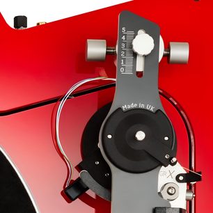 Nærbillede set ovenfra af Vertere Acoustics Pack Raw DGX hi-fi pladespiller i rød, med rød lakeret chassis, mørkegråt metalstativ med skala “0-5” og påskriften “Made in UK”, lysegrå cylindriske drejeknapper og et bundt flerfarvede ledninger