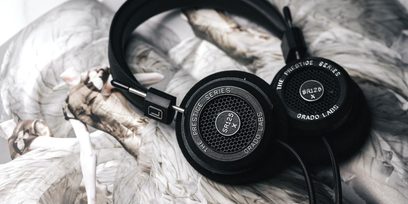Åben hi-fi hovedtelefon Grado SR125x lagt på hvide fjer, set fra en trekvart vinkel, sorte transducere og hovedbøjle i sort læder