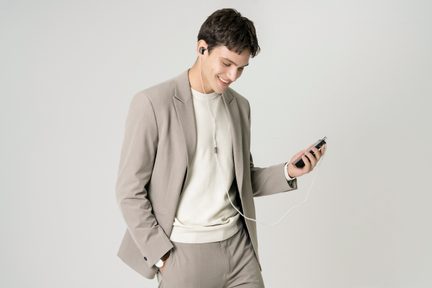 En mand i beige jakkesæt med en hvid sweater, høretelefoner i ørerne, holder en sort enhed med en hvid ledning