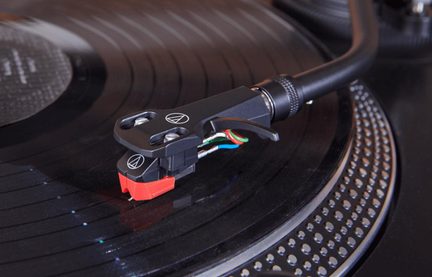 Testina phono Audio-Technica nera e rossa su braccio di giradischi in riproduzione, ripresa in primo piano
