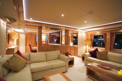 Luksuriøst interiør i en yacht med beige sofaer, røde puder, træbordplade, indbygget fladskærm og stemningsfuld belysning