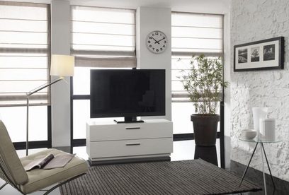 Bílý TV stolek se 2 zásuvkami, televizní obrazovka, zelená rostlina, nástěnné hodiny, stolní lampa a fotorámečky v obývacím pokoji