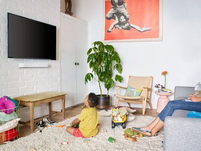 Stue med børn, der leger på et tæppe, grønne planter, lyse trævæggene, farverige puder, moderne kunstværk på væggen