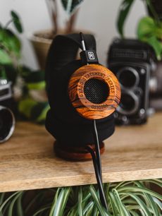 Åben hi-fi hovedtelefon Grado GS3000e i træ, set forfra på træsokkel, med grøn plante i baggrunden