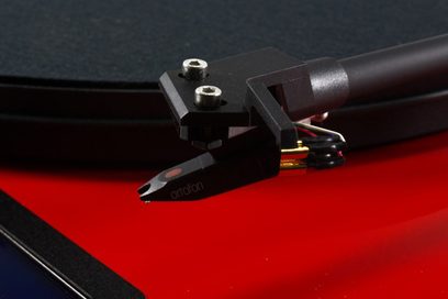 Hi-fi platenspeler Juke Box E1 rood gelakt, close-up van een zwarte cartridge met vergulde connectoren en gekleurde kabels