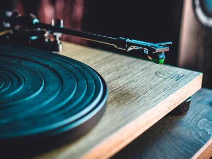 Audio-Technica pladespiller med sort tallerken og lyst træchassis, nærbillede af tonearmen og den grønne pickup