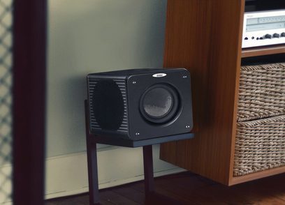 Velodyne MicroVee X sort subwoofer i sort, set forfra, placeret på et træmøbel ved siden af et hi-fi-møbel