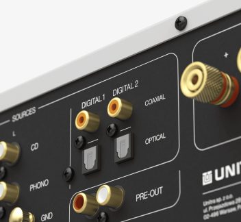 Bakpanel av lydforsterker i sort metall, gullfargede koaksiale RCA-kontakter og optiske TOSLINK-porter, sett fra siden