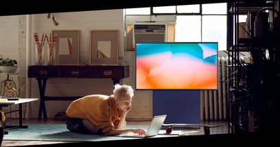 Samsung The Sero QE43LS05T-tv, der viser orange skyer, står på et møbel i et rum med et barn, der sidder foran på et tæppe og bruger en bærbar computer