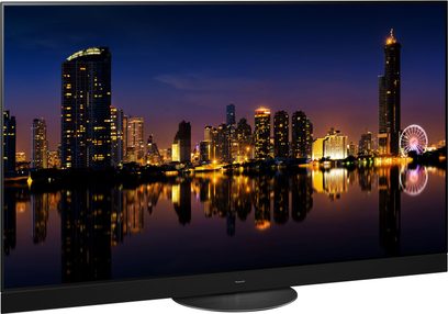 Téléviseur Panasonic TX-65MZ1500E affichant une vue nocturne de gratte-ciels illuminés et leurs reflets dans l'eau