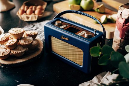 Retro blå bærbar radio i kunstlæder med gylden metalhøjttalergitter, række af hvide knapper, to store drejeknapper og øverste håndtag, set i trekvarts fugleperspektiv