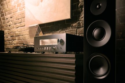 Sudraba hi-fi pastiprinātājs no matēta metāla, skatīts trīs ceturtdaļu leņķī, ar izgaismotiem VU mērītājiem un pogām, vinila atskaņotājs un melns skaļrunis