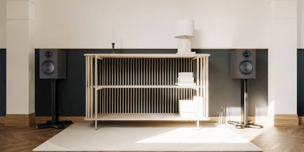 Consolemeubel met latten in licht hout met open planken, tussen twee zwarte luidsprekers op voet