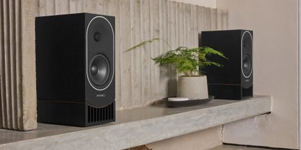 Svarta rektangulära PMC-hyllhögtalare med rund basdriver och frontport på en designad betonghylla