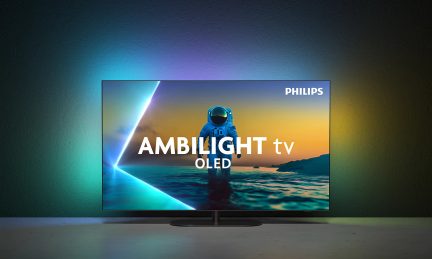 Svart platt-TV med tunn metallram sedd framifrån, monterad på ett ovalt centralt stativ, skärmen är påslagen och visar en astronaut med texten ”PHILIPS” omgiven av en flerfärgad ljushalo på väggen