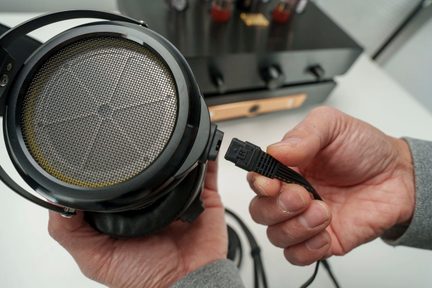 Fekete hi-fi fejhallgató kör alakú ráccsal, levehető kábelcsatlakozás közeli nézetben